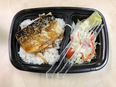 Plastik kaptaki pirinç kasesinin üstünde teriyaki sosuyla kızartılmış Saba balığı. 