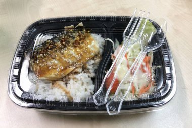 Plastik kaptaki pirinç kasesinin üstünde teriyaki sosuyla kızartılmış Saba balığı. 