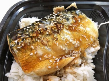 Plastik kaptaki pirinç kasesinin üstünde teriyaki sosuyla kızartılmış Saba balığı. 