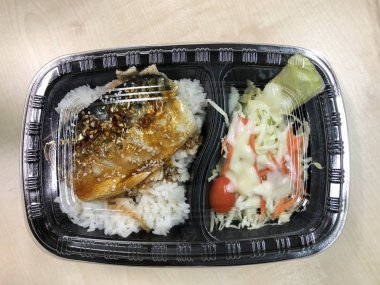 Plastik kaptaki pirinç kasesinin üstünde teriyaki sosuyla kızartılmış Saba balığı. 