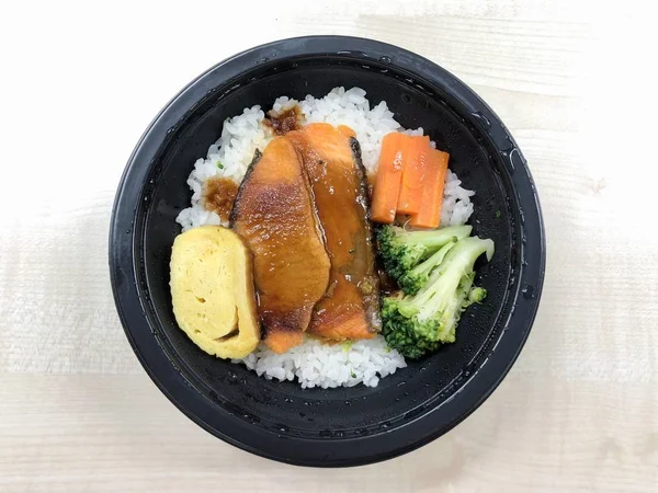 Salmon grilled with rice in the food container on the table