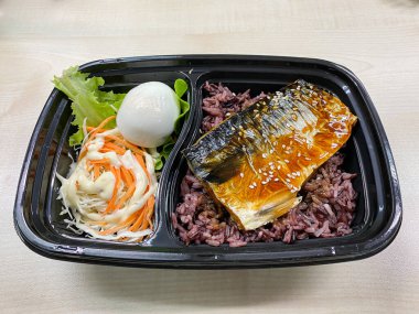 Plastik kaptaki pirinç kasesinin üstünde teriyaki sosuyla kızartılmış Saba balığı.
