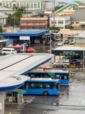 Bangkok, Tayland - 8 Eylül 2025: yağmurlu bir günde mavi halk otobüsleri istasyonun önüne park edildi. Banliyö sakinleri yürürken, motosikletler geçerken ve arka planda birkaç minibüs ve araba görüldü..