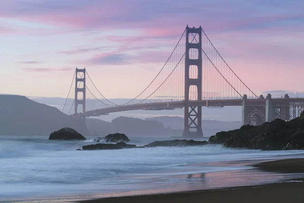 Classic panoramic view of famous Golden Gate Bridge seen from scenic Baker Beach in beautiful golden evening light on a sunset with blue sky and clouds in summer, San Francisco, California, USA