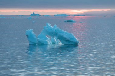 Arctic nature landscape with icebergs in Greenland icefjord with midnight sun sunset / sunrise in the horizon. Early morning summer alpenglow during midnight season. Ilulissat, West Greenland. clipart