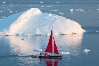 Küçük kırmızı yelkenli polar yaz gece yarısı güneş sezonu sırasında Disko Bay buzul yüzen buzdağları arasında seyir. Ilulissat, Grönland. Antarktika denizinde buzdağı ile sefer gemisi
