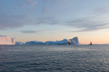 Buzdağları arasında küçük bir tekne. Gece yarısı güneşilulissat sırasında Disko Körfezi buzul yüzen buzdağları arasında seyir yelkenli Ilulissat, Grönland. Küresel ısınma buzve buzdağları fenomeninin incelenmesi