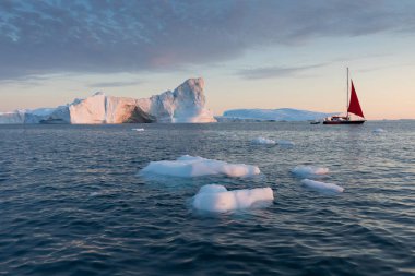 Buzdağları arasında küçük bir tekne. Gece yarısı güneşilulissat sırasında Disko Körfezi buzul yüzen buzdağları arasında seyir yelkenli Ilulissat, Grönland. Küresel ısınma buzve buzdağları fenomeninin incelenmesi