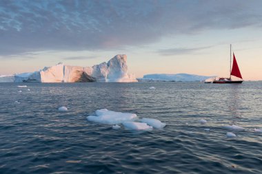 Buzdağları arasında küçük bir tekne. Gece yarısı güneşilulissat sırasında Disko Körfezi buzul yüzen buzdağları arasında seyir yelkenli Ilulissat, Grönland. Küresel ısınma buzve buzdağları fenomeninin incelenmesi