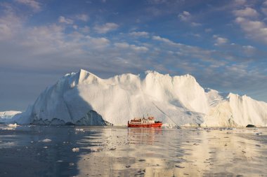 Buzdağları arasında küçük bir tekne. Gece yarısı güneşilulissat sırasında Disko Körfezi buzul yüzen buzdağları arasında seyir yelkenli Ilulissat, Grönland. Küresel ısınma buzve buzdağları fenomeninin incelenmesi