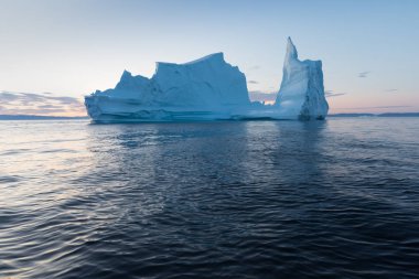 Gün batımında ilginç ve mavi bir gökyüzü altında fotojenik ve karmaşık buzdağı. Doğada küresel ısınmanın etkisi. Antarktika veya Grönland'da derin mavi suda eriyen buzulun kavramsal görüntüsü
