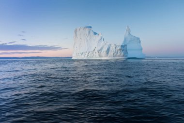 Gün batımında ilginç ve mavi bir gökyüzü altında fotojenik ve karmaşık buzdağı. Doğada küresel ısınmanın etkisi. Antarktika veya Grönland'da derin mavi suda eriyen buzulun kavramsal görüntüsü