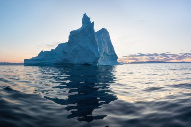 Gün batımında ilginç ve mavi bir gökyüzü altında fotojenik ve karmaşık buzdağı. Doğada küresel ısınmanın etkisi. Antarktika veya Grönland'da derin mavi suda eriyen buzulun kavramsal görüntüsü
