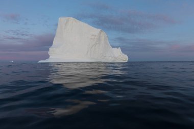 Gün batımında ilginç ve mavi bir gökyüzü altında fotojenik ve karmaşık buzdağı. Doğada küresel ısınmanın etkisi. Antarktika veya Grönland'da derin mavi suda eriyen buzulun kavramsal görüntüsü