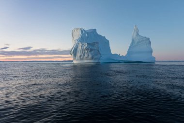 Gün batımında ilginç ve mavi bir gökyüzü altında fotojenik ve karmaşık buzdağı. Doğada küresel ısınmanın etkisi. Antarktika veya Grönland'da derin mavi suda eriyen buzulun kavramsal görüntüsü