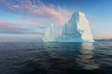 Gün batımında ilginç ve mavi bir gökyüzü altında fotojenik ve karmaşık buzdağı. Doğada küresel ısınmanın etkisi. Antarktika veya Grönland'da derin mavi suda eriyen buzulun kavramsal görüntüsü
