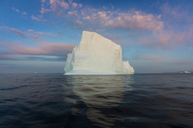 Gün batımında ilginç ve mavi bir gökyüzü altında fotojenik ve karmaşık buzdağı. Doğada küresel ısınmanın etkisi. Antarktika veya Grönland'da derin mavi suda eriyen buzulun kavramsal görüntüsü