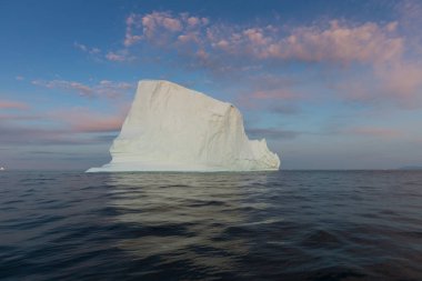 Gün batımında ilginç ve mavi bir gökyüzü altında fotojenik ve karmaşık buzdağı. Doğada küresel ısınmanın etkisi. Antarktika veya Grönland'da derin mavi suda eriyen buzulun kavramsal görüntüsü