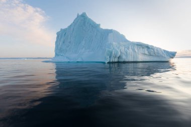 Gün batımında ilginç ve mavi bir gökyüzü altında fotojenik ve karmaşık buzdağı. Doğada küresel ısınmanın etkisi. Antarktika veya Grönland'da derin mavi suda eriyen buzulun kavramsal görüntüsü