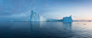 Gün batımında ilginç ve mavi bir gökyüzü altında fotojenik ve karmaşık buzdağı. Doğada küresel ısınmanın etkisi. Antarktika veya Grönland'da derin mavi suda eriyen buzulun kavramsal görüntüsü