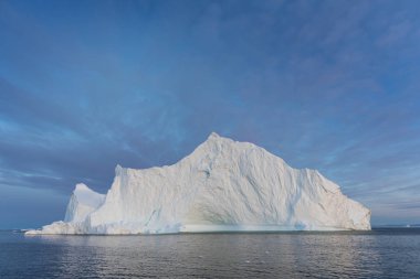 Gün batımında ilginç ve mavi bir gökyüzü altında fotojenik ve karmaşık buzdağı. Doğada küresel ısınmanın etkisi. Antarktika veya Grönland'da derin mavi suda eriyen buzulun kavramsal görüntüsü