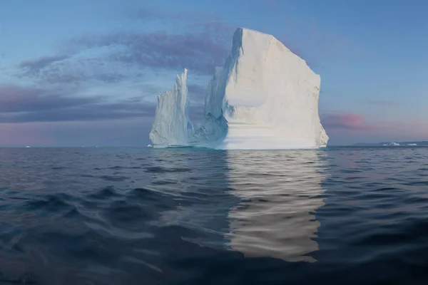 Photogenic and intricate iceberg under an interesting and blue sky during sunset. Effect of global warming in nature. Conceptual image of melting glacier in deep blue water in Antarctica or Greenland