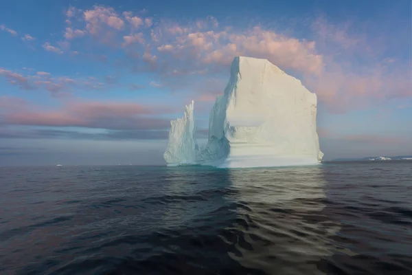 Photogenic and intricate iceberg under an interesting and blue sky during sunset. Effect of global warming in nature. Conceptual image of melting glacier in deep blue water in Antarctica or Greenland