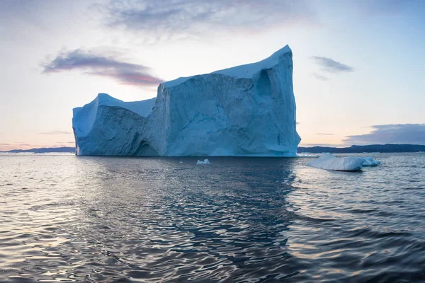 Photogenic and intricate iceberg under an interesting and blue sky during sunset. Effect of global warming in nature. Conceptual image of melting glacier in deep blue water in Antarctica or Greenland