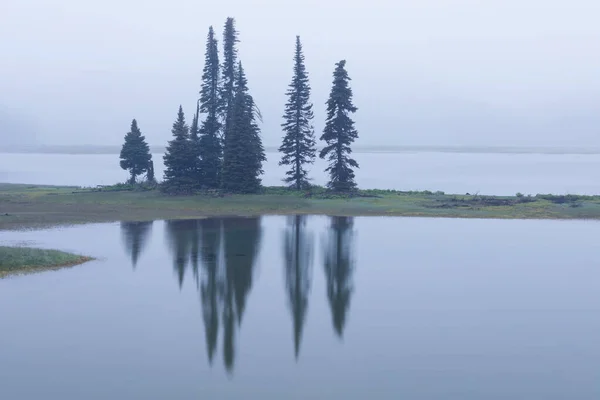 Sparks Lake at sunrise in the Cascades Range in Central Oregon, USA in an early morning light. Morning mist rises from lake into trees.