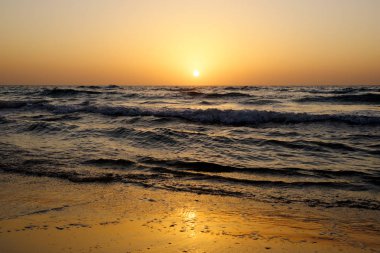 Dalgalar İsrail ile Akdeniz üzerinde bulutsuz gökyüzünde parlak bir günbatımı