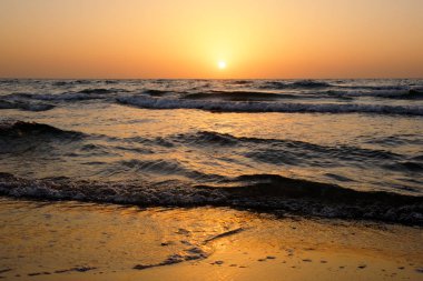 Dalgalar İsrail ile Akdeniz üzerinde bulutsuz gökyüzünde parlak bir günbatımı
