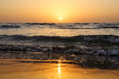 Dalgalar İsrail ile Akdeniz üzerinde bulutsuz gökyüzünde parlak bir günbatımı