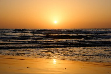 Dalgalar İsrail ile Akdeniz üzerinde bulutsuz gökyüzünde parlak bir günbatımı
