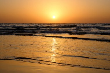 Dalgalar İsrail ile Akdeniz üzerinde bulutsuz gökyüzünde parlak bir günbatımı