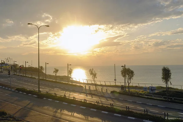 road near the Mediterranean Sea in Israel against the background of orange sunset and the cloudy sky