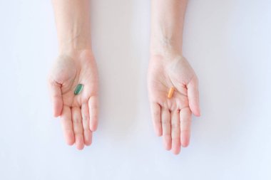 vitamin hapları ilaçlar biyolojik ellerde beyaz zemin üzerine yeşil ve turuncu oval tablet yalanımı takviyeleri