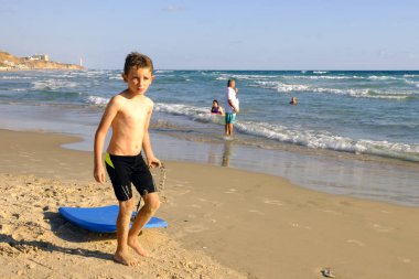 İsrail - Netanya beach, 12 Ekim 2017: çocuk sahilde sörf denize doğru sürükler.