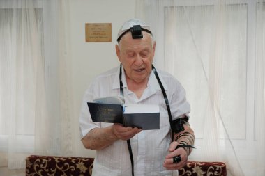 ISRAEL - Netanya, 23 May 2019: an elderly Jewish man puts on a tefillin before a prayer