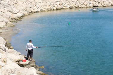 ISAREL - Herzliya, 29 Mayıs 2020: Akdeniz 'de uzun olta kamışlı beyaz tişörtlü bir balıkçı