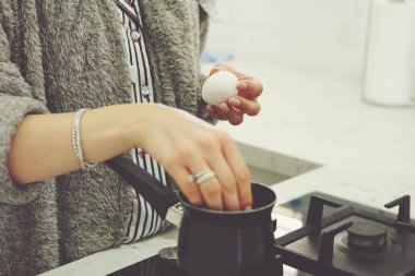 Kadın eli tavada pişirmek için yumurta koyar.