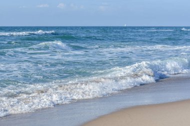 Deniz, mavi gökyüzünün altında beyaz köpük mavi dalgalar.