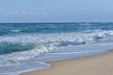 Deniz, mavi gökyüzünün altında beyaz köpük mavi dalgalar.