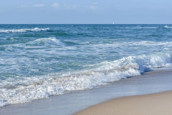 Deniz, mavi gökyüzünün altında beyaz köpük mavi dalgalar.