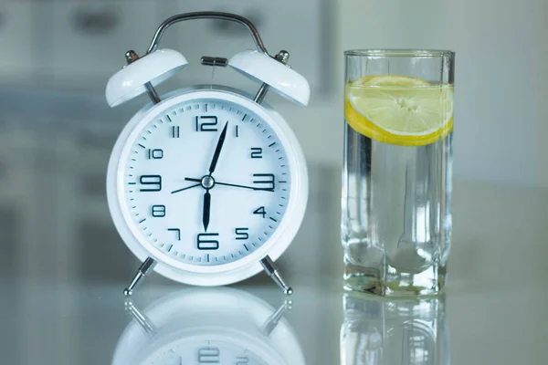 Väckarklocka och en detox glas vatten med citron på ett glas bord. Vakna tidigt på morgonen av väckarklockan — Stockfoto