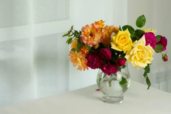 Beautiful Bouquet of summer orange yellow and purple English roses in glass vase, jar near the big white window on table. Royalty Free Stock Images