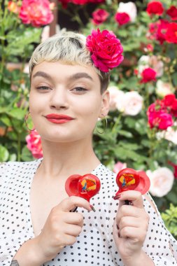 Beyaz bir bluz ve saçları bir gül ile güzel bir genç sarışın kız inanılmaz bir yaz arka planda bir gül bahçesinde duygularını ifade eder. Kız kırmızı castanets ile oynuyor.