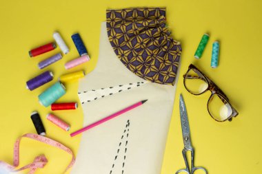 Bir yelow arka plan üzerinde dikiş aksesuarları ve kumaş. Dikiş iplikleri, pimleri, desen ve dikiş santimetre. Evde dikiş diktiğiiçin. Üst tenli, düzlük