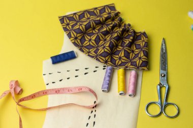 Bir yelow arka plan üzerinde dikiş aksesuarları ve kumaş. Dikiş iplikleri, pimleri, desen ve dikiş santimetre. Evde dikiş diktiğiiçin. Üst tenli, düzlük