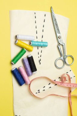 Bir yelow arka plan üzerinde dikiş aksesuarları ve kumaş. Dikiş iplikleri, pimleri, desen ve dikiş santimetre. Evde dikiş diktiğiiçin. Üst tenli, düzlük