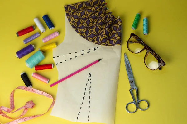 Bir yelow arka plan üzerinde dikiş aksesuarları ve kumaş. Dikiş iplikleri, pimleri, desen ve dikiş santimetre. Evde dikiş diktiğiiçin. Üst tenli, düzlük